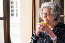 download (50) idoso segurando um copo de leite ao lado de uma janela ensolarada.