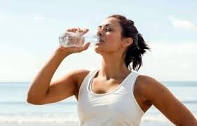 images (1) mulher hidratando-se na praia para prevenir infecção urinária no verão