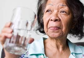 download (36) idoso segurando um copo de água, sinalizando sintomas discretos de desidratação.