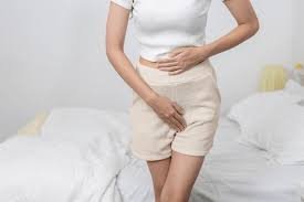 download (41) Mulher sentada segurando a região pélvica com expressão de desconforto