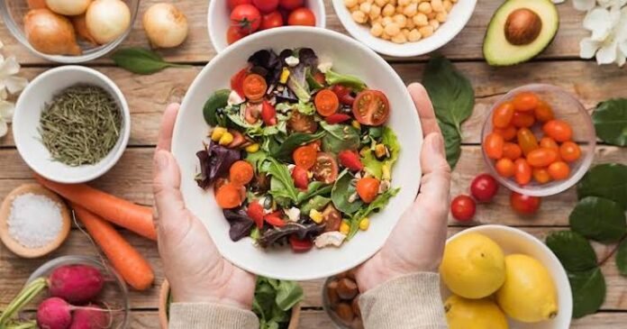 images Fotografia realista e horizontal mostrando uma alimentação equilibrada sobre uma mesa clara, com frutas, verduras, legumes, grãos integrais e um copo de água. A composição deve transmitir saúde intestinal e prevenção, sem desenhos anatômicos exagerados.